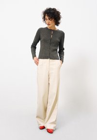 Grauer Strickcardigan mit Rundhalsausschnitt und Knopfverschluss, kombiniert mit lockeren cremfarbenen Hosen und roten Absätzen. Glattes Material, entspannter Schnitt.