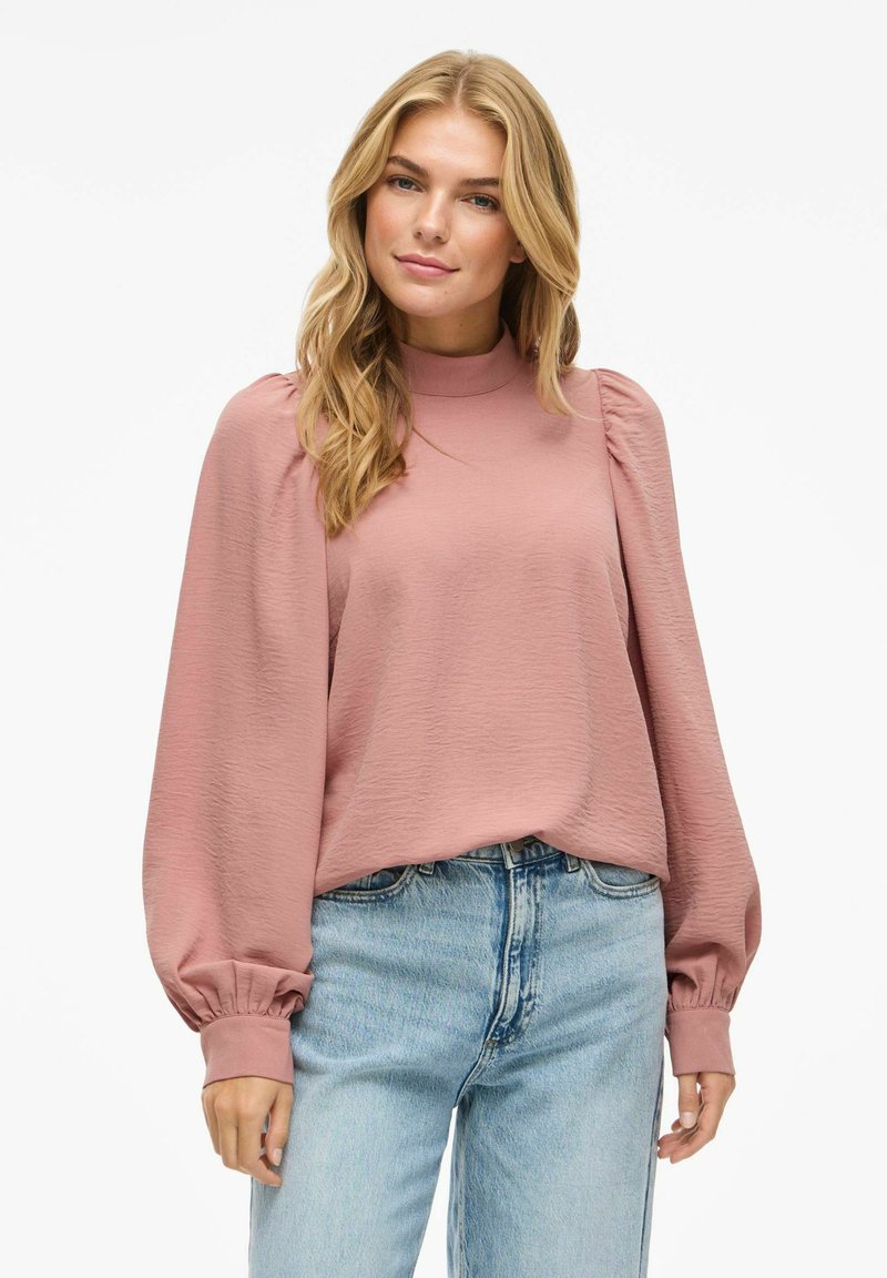 Rosa texturerad blus med hög krage och puffade långa ärmar, tillsammans med ljusblå denimjeans. Lätt, luftig tyg.