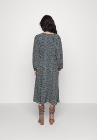 Kukkakuosiset mekko pitkillä hihoilla, löysällä istuvuudella ja polvipituisella helmalla. Tumma tausta, jossa on pieniä sinisiä ja keltaisia kukkia.