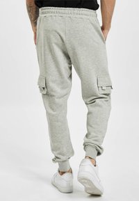 Graue Sweatpants mit lockerer Passform, ausgestattet mit zwei seitlichen Cargo-Taschen und gerippten Bündchen. Kombiniert mit weißen Sneakern.