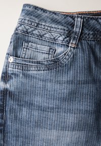 Jeans in denim blu chiaro con una texture a costine diagonali, cinque tasche e cuciture arancioni lungo la vita.