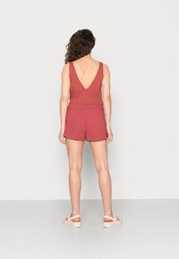 Bodysuit sin mangas de color rojizo con un profundo escote en la espalda, combinado con pantalones cortos a juego. Tejido ligero y texturizado, con cinturilla elástica.