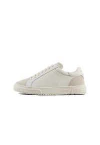 Zapatillas de deporte beige claro, hechas de cuero y ante, con puntera redonda, cordones planos y una suela de goma texturizada con marca en el lado.