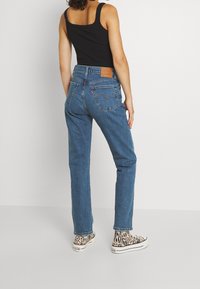 Vaqueros de tiro alto en azul con corte recto clásico, que presentan un parche de cuero marrón, bolsillos traseros y zapatillas con estampado animal.