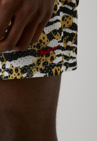 Nike šortai, pasižymintys geltonai, juodai ir baltai gyvūnų rašto motyvu, su raudonu logotipo akcentu. Pagaminti iš kvėpuojančios medžiagos su tekstūruotu paviršiumi.