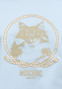 Γάτα που φοράει στρογγυλά γυαλιά και φιόγκο, πλαισιωμένη από κύκλο σχοινιού, με την επιγραφή «MOSCHINO JEANS» κάτω σε ανοιχτό γαλάζιο φόντο.