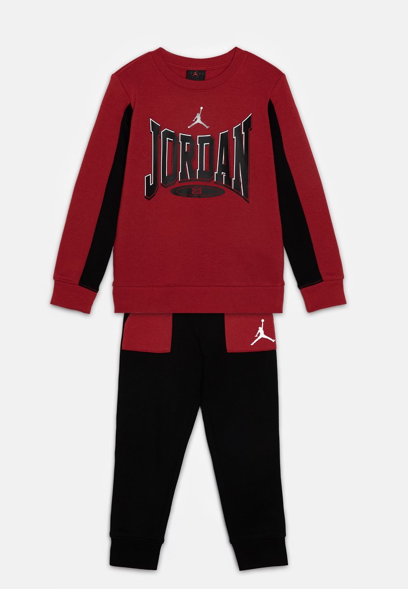 Felpa rossa con stampa "JORDAN" e dettagli neri, abbinata a pantaloni neri con tasche rosse e dettaglio del logo bianco.