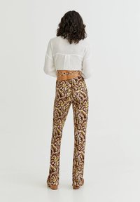 Spodnie w kształcie dzwonów w wielokolorowy kwiatowy wzór w brązowym, różowym i zielonym kolorze. Miękka, gładka tkanina. Z tyłu znajduje się dopasowany pas z wiązaniami.