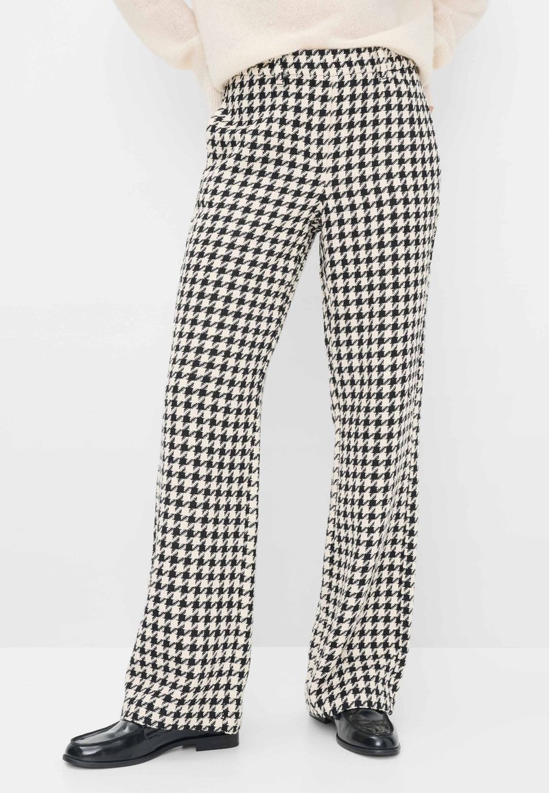Zwart-wit houndstooth patterne broek met een losse pasvorm, voorzien van een elastische tailleband en textuur stof, gecombineerd met zwarte schoenen.