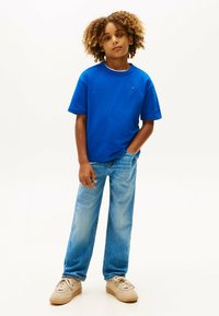 T-shirt in cotone blu con colletto rotondo, abbinata a jeans in denim blu chiaro. Calzature in sneakers beige. Presenta una texture morbida e una vestibilità rilassata.