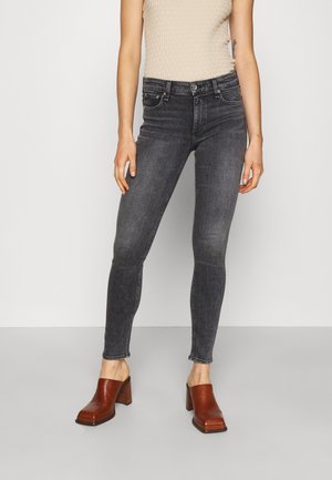 Jean skinny gris foncé avec une taille haute, comportant cinq poches et une fermeture à bouton. Assorti avec des sabots bruns à talon bloc.