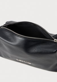 Bolsa de cuero negro con una apertura de cremallera plateada, que presenta una textura suave y un diseño minimalista. El interior está forrado con tela negra.