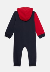 Un pyjama en coton bleu marine et rouge avec des manches longues, une capuche et des poignets côtelés. Il présente un corps bleu marine uni et une capuche rouge, conçu pour les nourrissons.