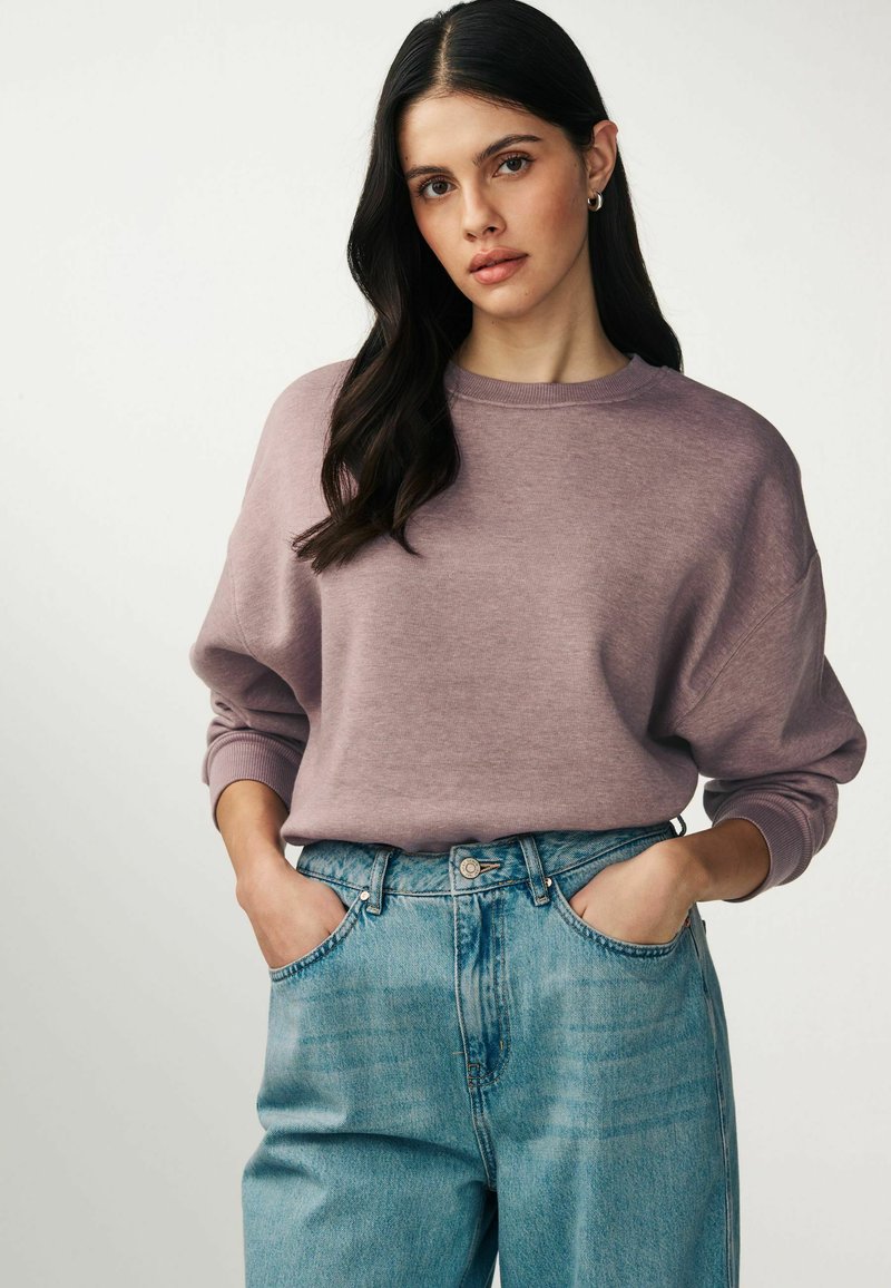 Lillasest oversized pusak, millel on soonilised mansetid, koos kõrge vöökoha ja helesiniste teksadega. Pehme tekstuur ja mugav lõige.