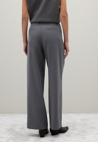 Grijze broek met wijde pijpen van textuurstof, met achterzakken en een getailleerde pasvorm. Gecombineerd met zwarte haklaarzen.