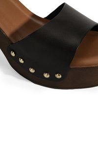 Zwarte leren wedge sandaal met een brede band, tan voetbed en contrasterende gouden studs als detail langs de rand van de buitenzool.