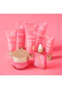 Otto prodotti per la cura della pelle NUXE Prodigieuse Boost in tubi e barattoli rosa, con dettagli dorati e varie texture, disposti su uno sfondo rosa.