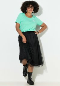 Lysegrøn kortærmet t-shirt med solmotiv, kombineret med en sort tylskørt. Sorte ankelstøvler med nitter fuldender outfittet.