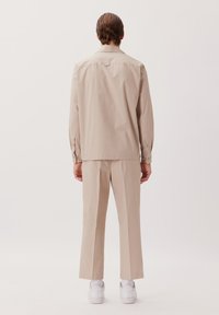 Ensemble chemise et pantalon beige en tissu tissé, avec une coupe droite, des manches longues et des baskets blanches. Design minimaliste sans motif.