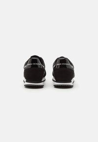 Černé semišové a síťované tenisky s bílou podrážkou. Reflexní akcenty s logem "ARMANI EXCHANGE" na patě. Minimalistický design.