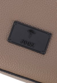 Brun tekstureret læderpung med et sort præget mærke med "JOOP!" og et dekorativt motiv. Glat og holdbar overflade.