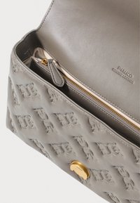 Borsa a mano in pelle grigia con design impresso, hardware in oro e tasca con zip interna. Texture liscia e linee pulite. Logo del marchio visibile.
