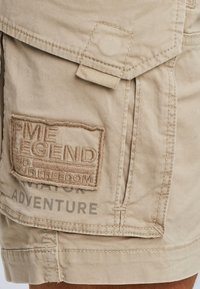 Kahki cotton shorts featuring a textured patch with "PME LEGEND" embroidered, and printed text detailing "ADVENTURE" on the side.