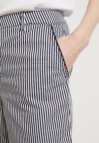 Námořnicky modré a bílé proužkované kalhoty s hladkou texturou. Mají pas, boční kapsu a upravený střih.