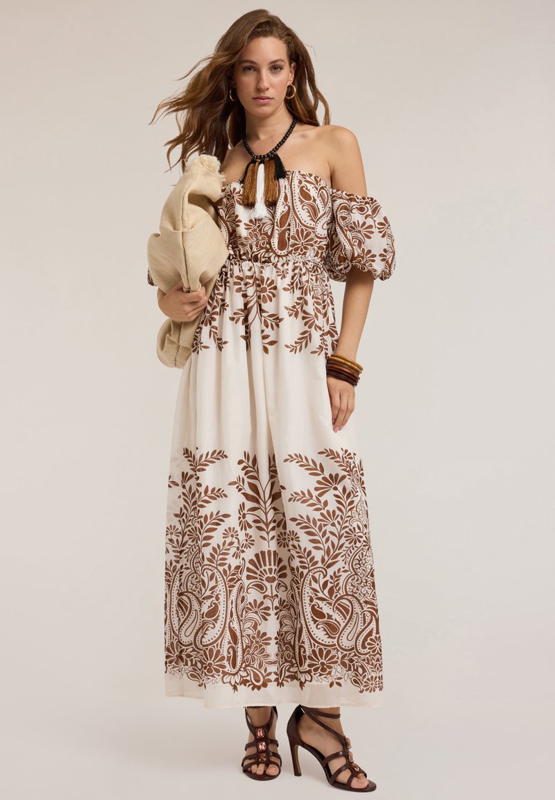Robe maxi en coton blanc avec des motifs floraux marron. Dotée de manches bouffantes dénudées sur les épaules, d'une taille élastique et d'une jupe fluide.