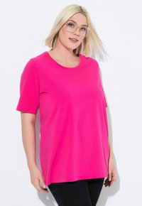T-shirt a maniche corte, collo a giro, in tessuto rosa brillante, con una vestibilità ampia e una texture morbida. Indossato con pantaloni neri.