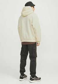 Fuzzy creme hoodie med en tætsiddende pasform, parret med sorte cargobukser med sidelommer og manchetter. Sorte sneakers med grå detaljer.