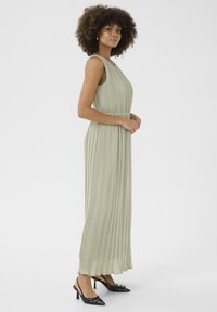 Fållad, lång klänning i ljusgrön med ärmlös design. Matchas med svarta spetsiga klackar med en accentdetalj.