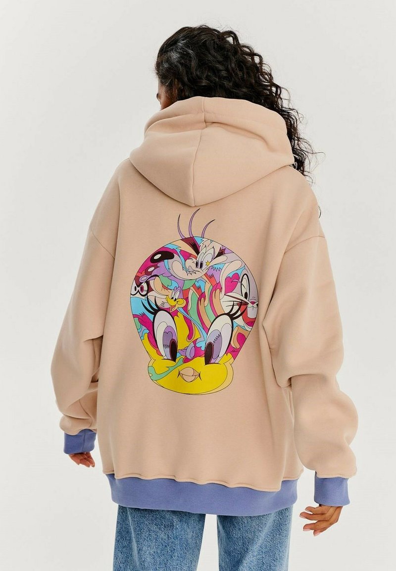 Veľká béžová mikina s kapucňou so živou karikatúrnou grafikou na chrbte, ktorá zobrazuje postavy v okrúhlom dizajne. Pružné modré manžety na rukávoch.