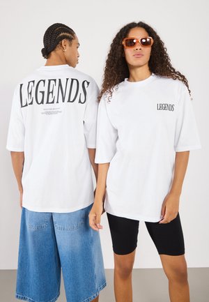T-shirts blancs surdimensionnés avec "LEGENDS" imprimé au dos et à l'avant, associés à des shorts en denim et des shorts de cyclisme noirs.