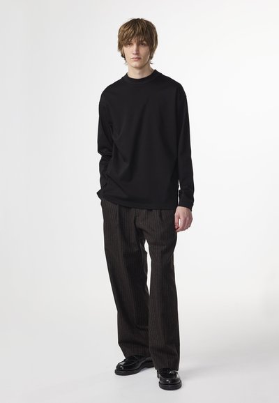 Black long-sleeve shirt paired with pinstriped dark brown wide-leg trousers and black shoes. The outfit has a relaxed fit and minimal design.