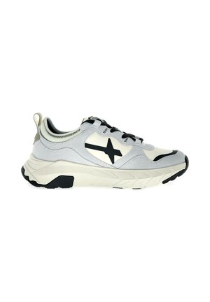 Zapatilla deportiva blanca y gris con estrella negra en el lateral, cordones negros, suela beige gruesa y banda negra en el talón y la puntera.