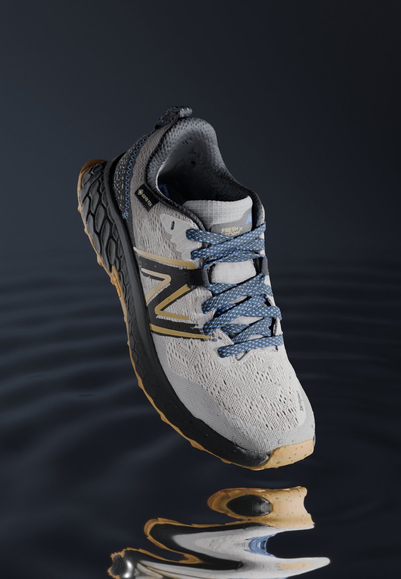 Zapatilla de running gris con parte superior de malla texturizada, cordones azules, acentos dorados y suela negra. Cuenta con la tecnología Fresh Foam para mayor amortiguación.