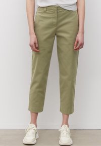 Olijf groene katoenen broek, cropped lengte, rechte snit, platte voorkant met riemlussen, gecombineerd met witte sneakers en een simpel T-shirt.