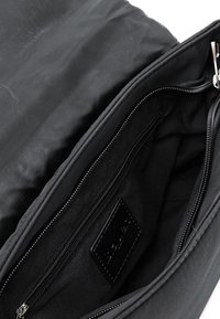 Borsa di stoffa nera aperta per mostrare l'interno con una tasca con cerniera e un'etichetta nera all'interno.