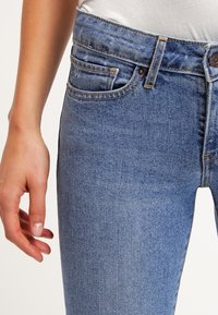Ljusblå denimjeans med hög midja, fem fickor och kontrasterande sömmar. Tyget har en lätt strukturerad yta med en klassisk passform.