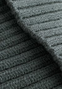 Tissu gris foncé texturé avec un motif côtelé, mettant en valeur une structure douce et tissée. Le matériau semble épais et confortable.