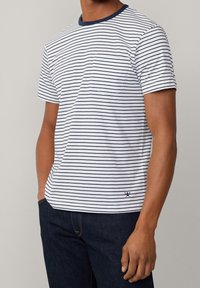 Striped short-sleeve T-shirt in white and navy, featuring a crew neck, single chest pocket, and a relaxed fit. Fabric has a smooth texture.