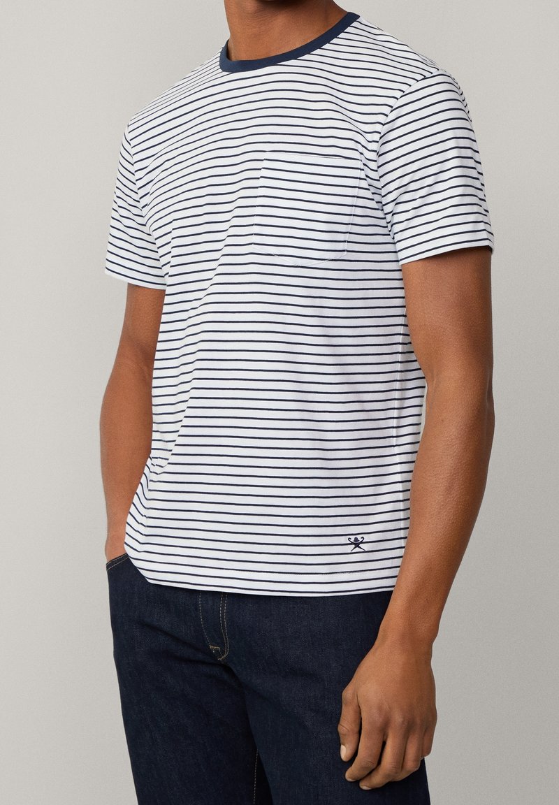 Striped short-sleeve T-shirt in white and navy, featuring a crew neck, single chest pocket, and a relaxed fit. Fabric has a smooth texture.