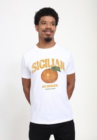 Bílá bavlněná tričko s grafickým potiskem pomeranče, na kterém je v žlutém textu nápis "SICILIAN" a pod ním v zeleném textu "arancia frutta fresca".