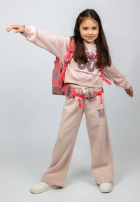 Felpa rosa chiaro con la scritta "New York 80", abbinata a pantaloni larghi coordinati. Gli accenti grigi sullo zaino e sulle sneakers aggiungono contrasto.