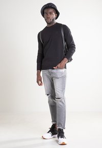 Czarny sweter, szare podarte dżinsy, czarny kapelusz typu bucket oraz czarno-białe sneakersy. Strój cechuje się casualowym stylem i luźnym krojem.