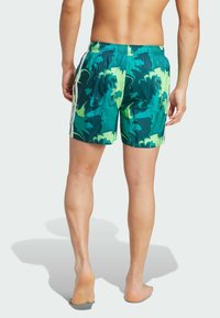 Zelené a žlté vzorované plavkové šortky s elastickým pásom, bočnými pruhmi a strednou dĺžkou, navrhnuté pre pohodlie a pohyb.