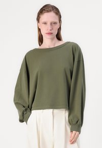 Olíva zöld, hosszú ujjú, oversize pulóver széles nyakkal és rugalmas mandzsettákkal, puha pamut anyagból készült, deréknál szegélyezve.