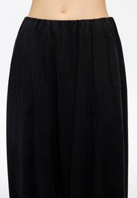 Czarne szerokie spodnie z miękkiego materiału; posiadają elastyczną gumkę w pasie i pionowe szwy nadające strukturę.