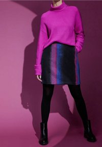 Pull en maille côtelée fuchsia avec un col haut, associé à une jupe noire avec des rayures multicolores verticales. Des bottines noires à la cheville complètent le look.